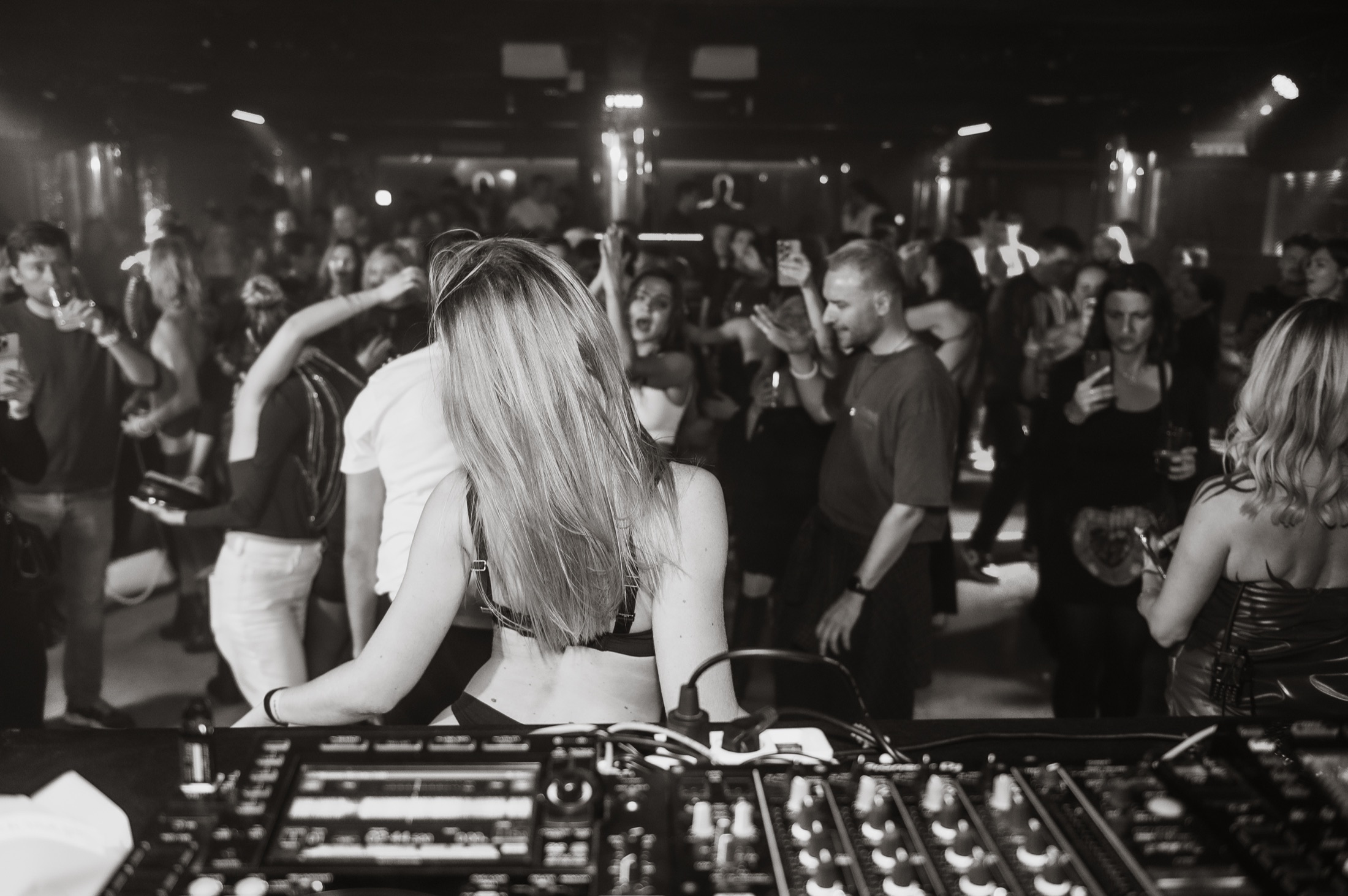 DJ facing a crowded dance floor, photographed in black and white