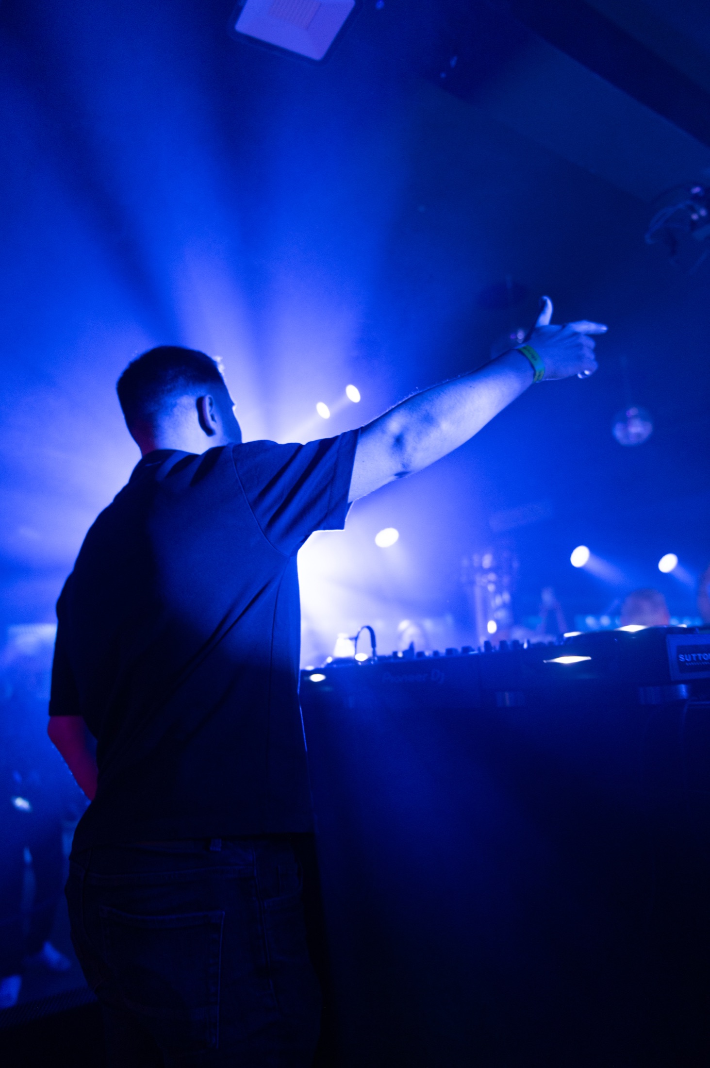 DJ reaching towards the crowd through deep blue light